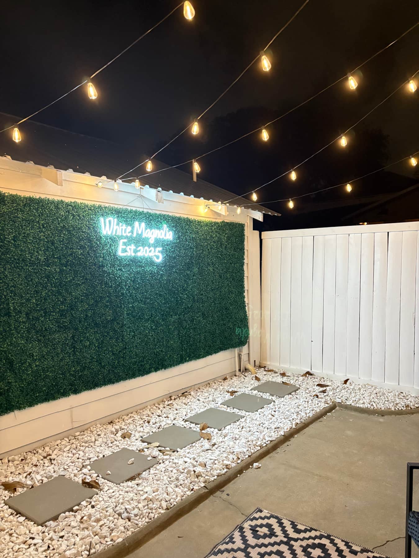 Illuminated White Magnolia logo photo wall in the private courtyard.