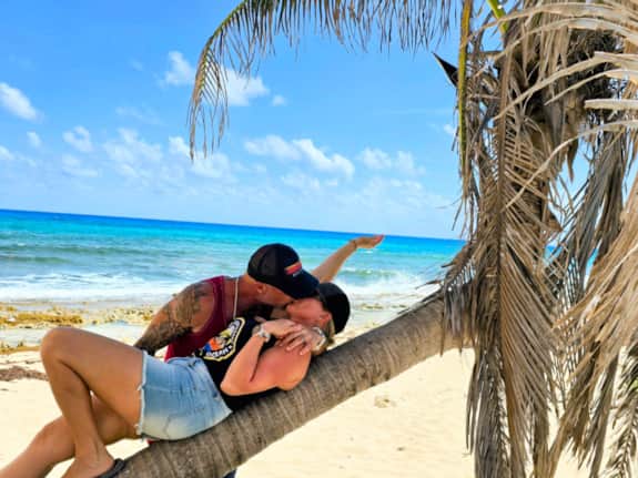 A couple enjoying the wild east coast of Cozumel beside a palm tree and turquoise Caribbean water