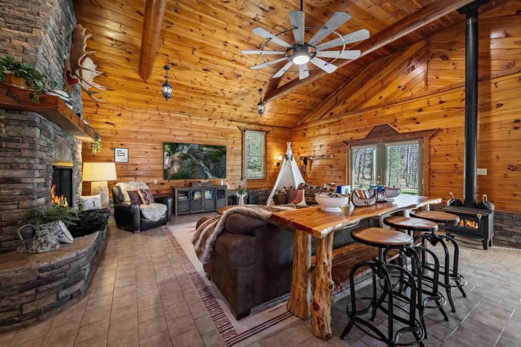 85” Smart TV, cozy sectional seating, and a high top live-edge table with stools + a separate wood carved high-top table & 4 chairs.