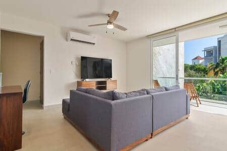 Cozy living room with plush couch, smart TV, AC, fan & balcony access.