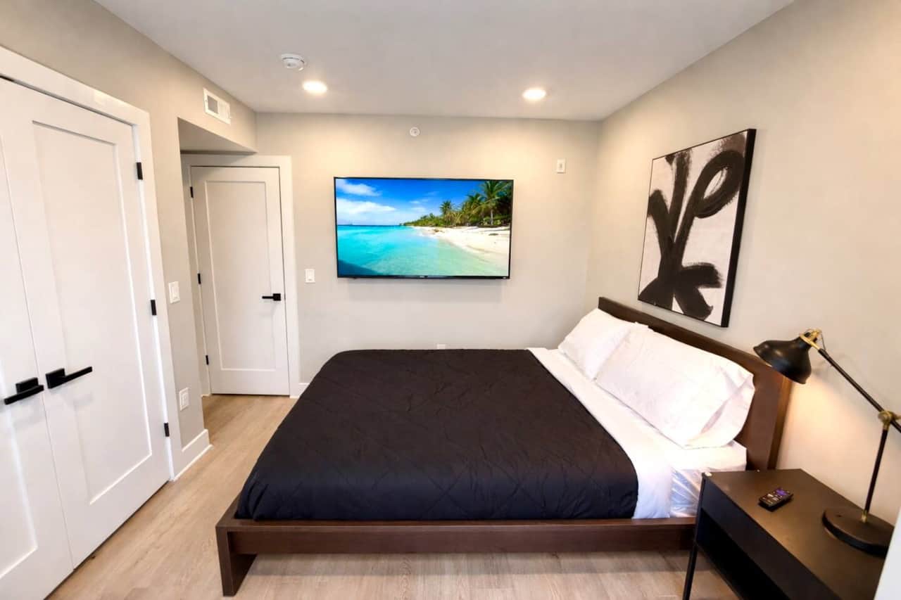 This modern bedroom features a comfortable queen-size bed, a large closet for extended stays, and a w flat-screen TV. Designed with a clean, contemporary style, the room offers a calm and comfortable space to relax, work, or unwind after a long day.
