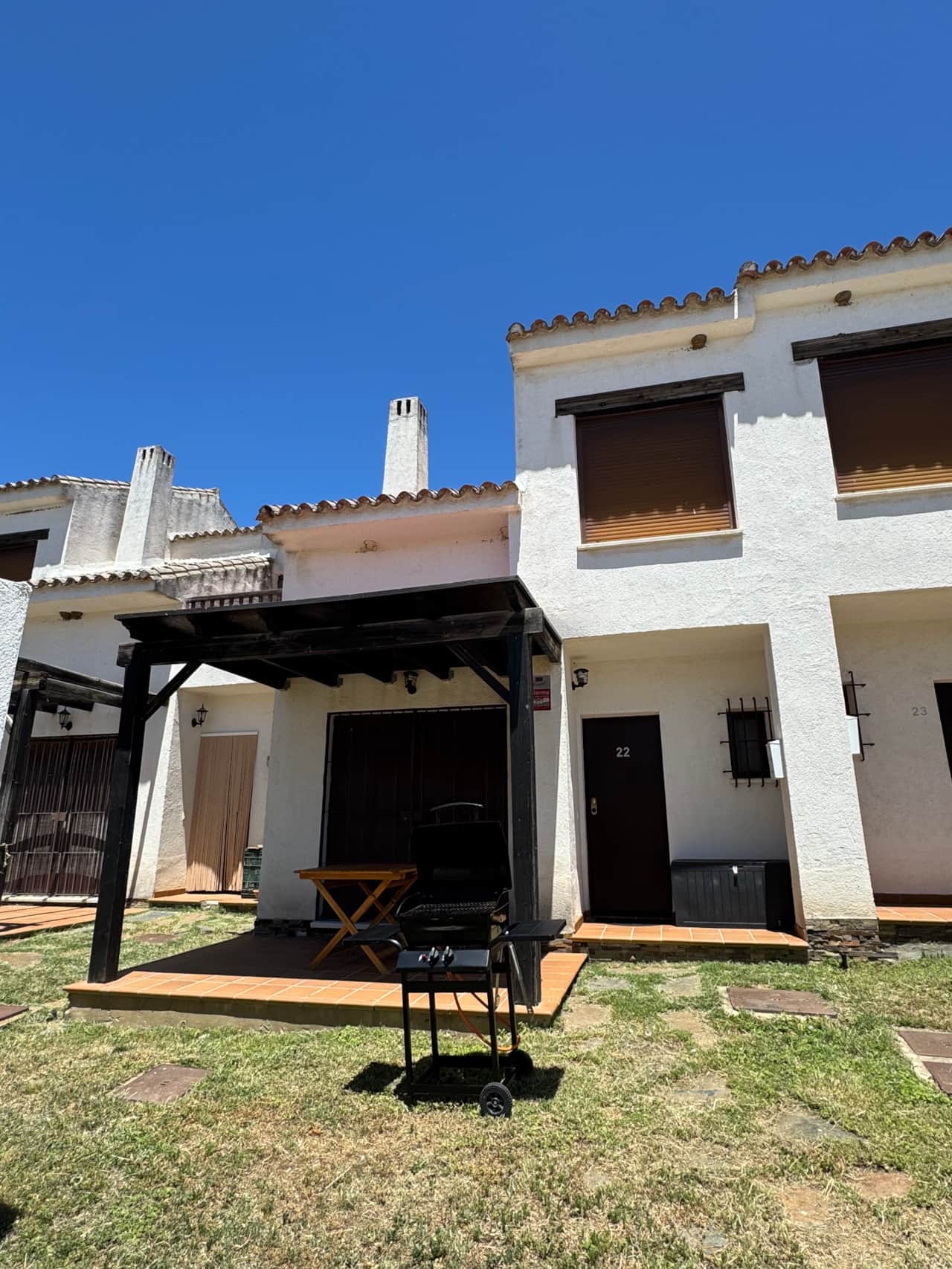 Fachada de la casa con porche, césped y barbacoa