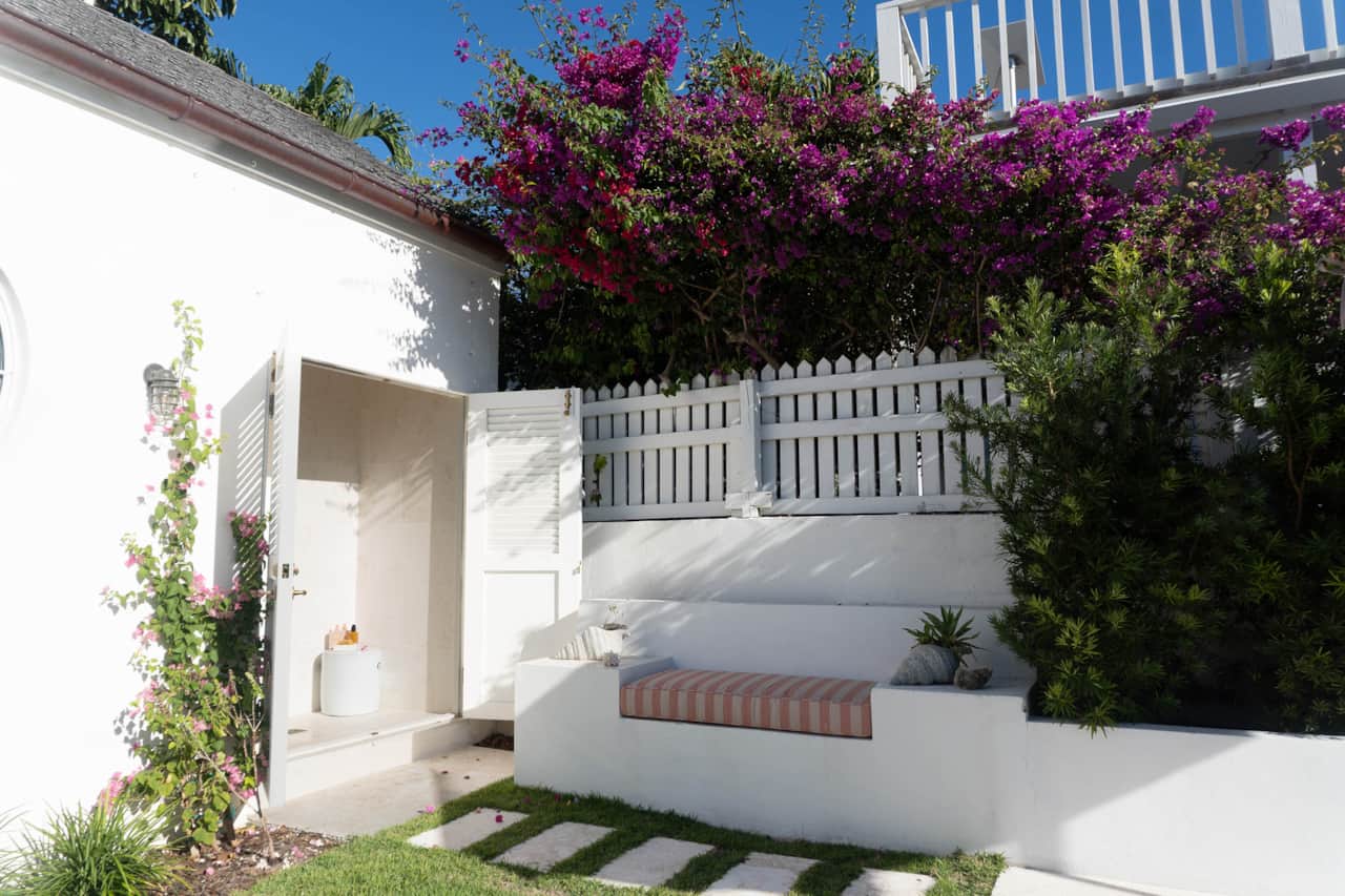 Open outdoor shower enclosure and a built-in white bench with a striped cushion, framed by a white p