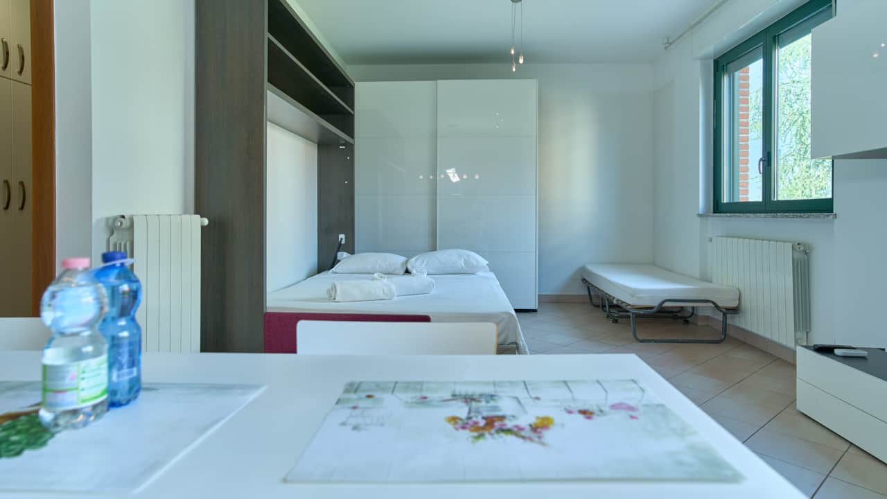 Dormitorio luminoso con cama y ventanas al verde, en Monza