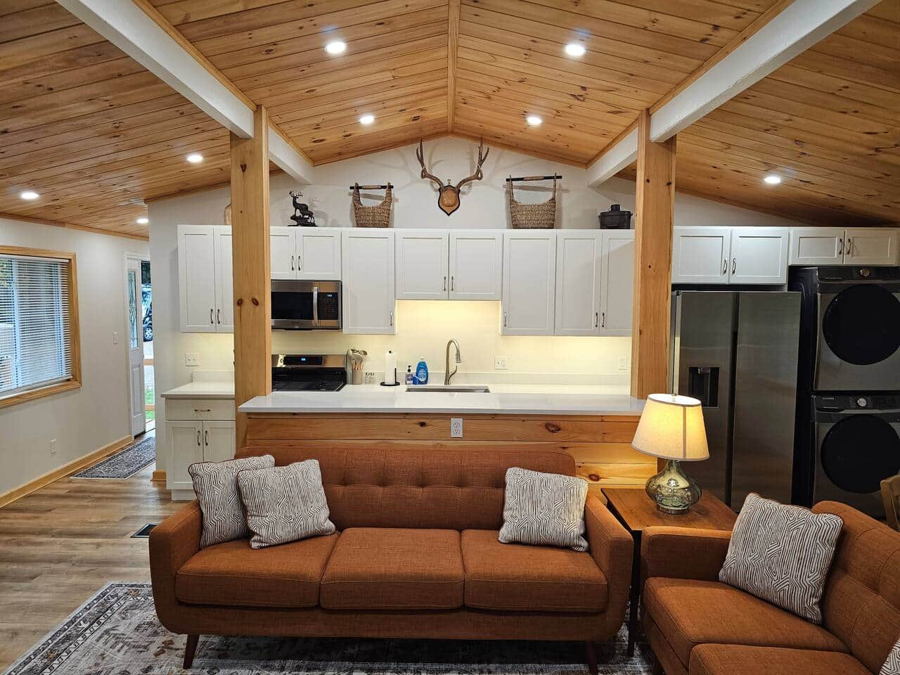 Step into a bright, modern-rustic space with a tongue-and-groove ceiling, warm beams, and dimmable lighting. Enjoy quartz counters, white cabinetry, stainless appliances, and mid-century sofas in the open living area.