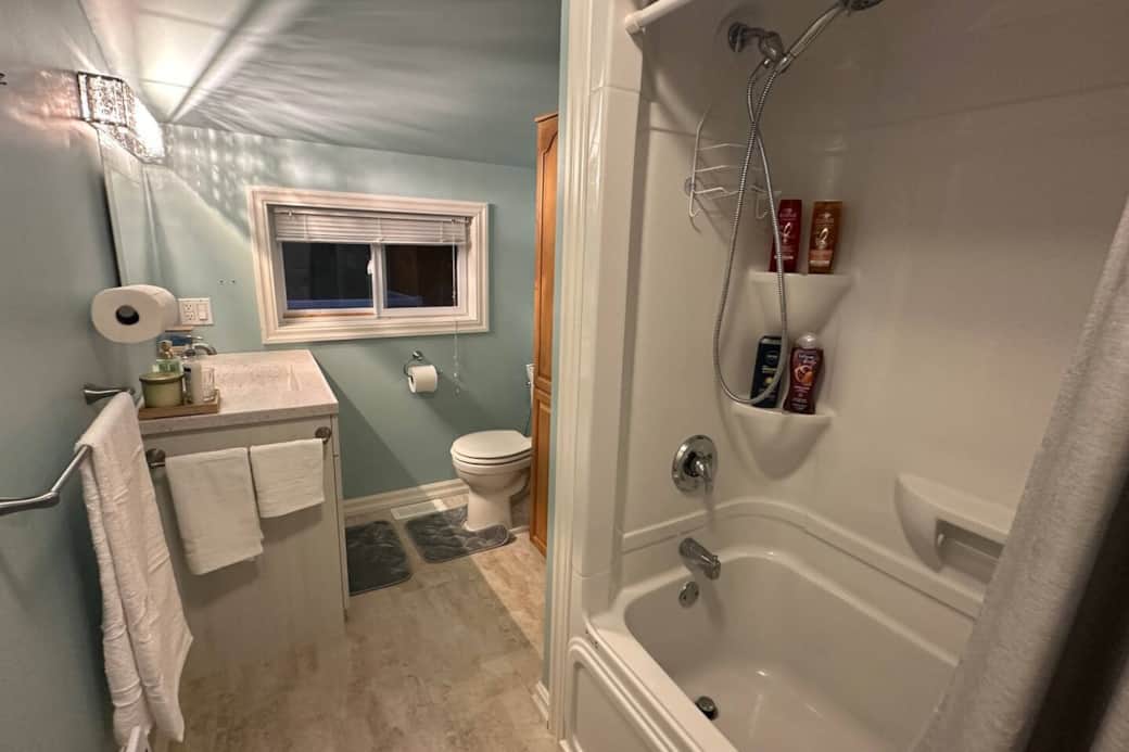 Bright and spotless full bathroom with a shower–tub combo, fresh towels, and complimentary toiletries. 