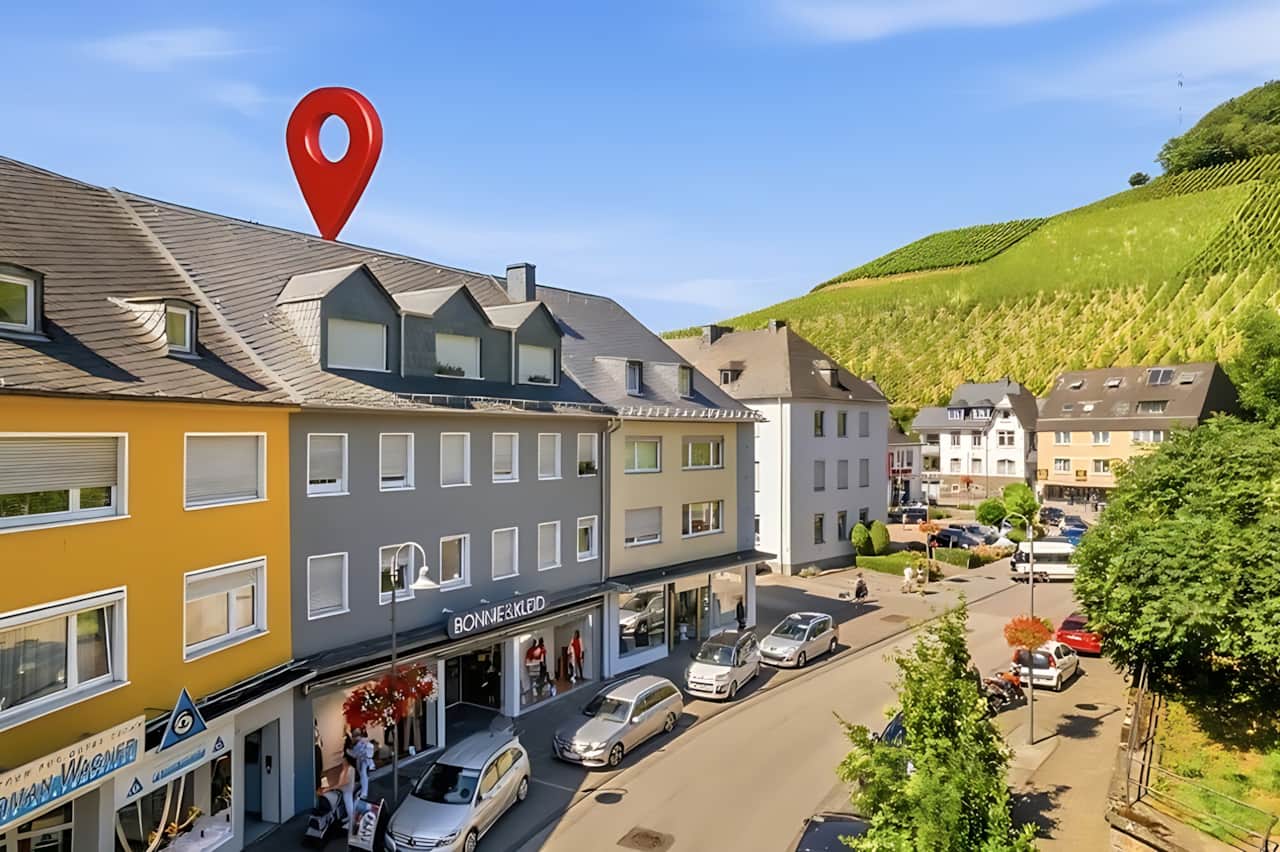 Luftaufnahme des Hauses in belebter Stadtlage, grüne Weinberge im Hintergrund, roter Standort-Pin ma