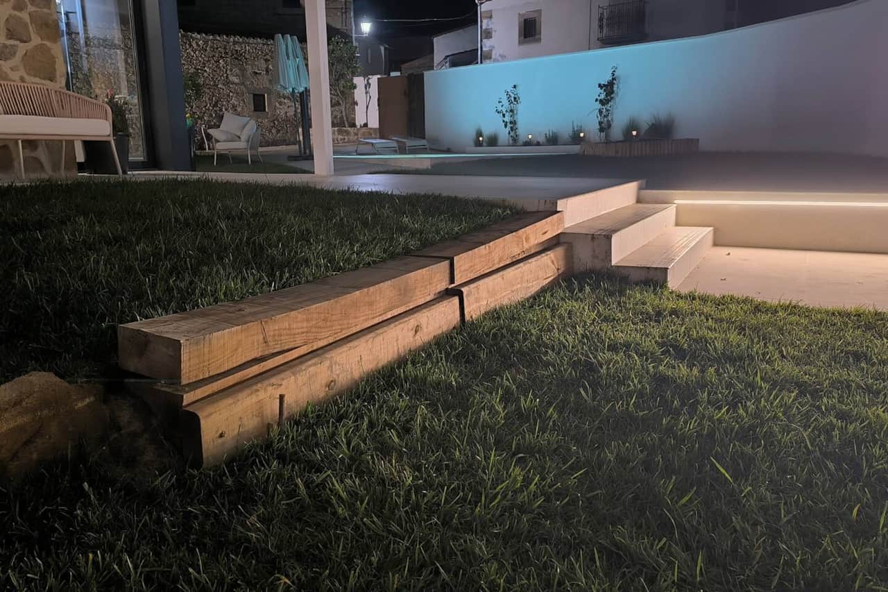 vista nocturna desde el pequeño patio a la izquierda de la entrada. Una luz led crea un ambiente muy acogedor en esta tranquila zona donde puedes descansar en el sofá de exterior bajo el porche delantero.