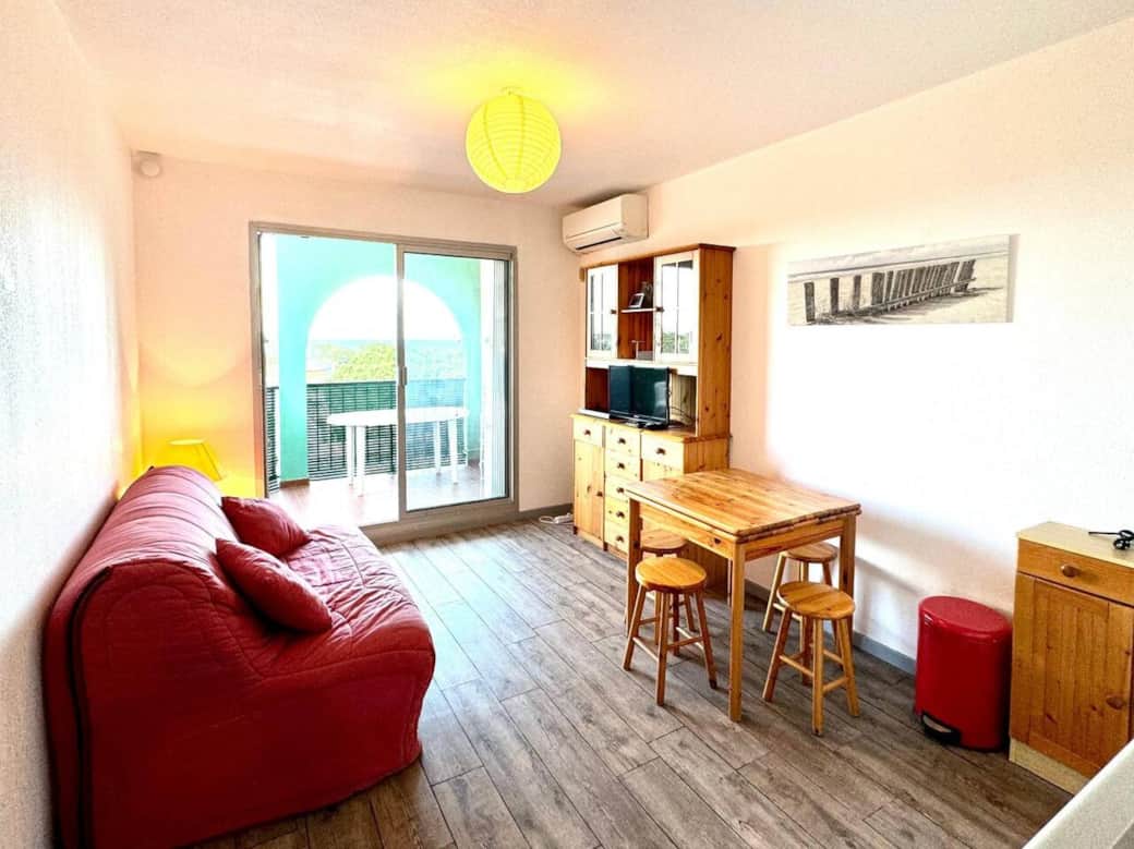 Séjour accueillant avec canapé, coin repas et climatisation, ouvert sur une loggia ensoleillée avec vue dégagée. Profitez d’un espace lumineux idéal avant de flâner au port d’Argelès, savourer ses restaurants et rejoindre la plage à pied.