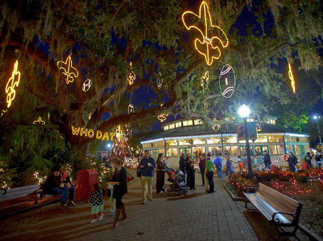 A large tree with festive lights and people walking around in a brick-paved area at night.