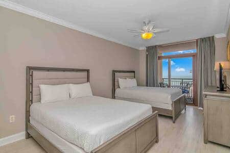 Large guest suite with two queen beds, flatscreen TV, and private balcony access with ocean views.