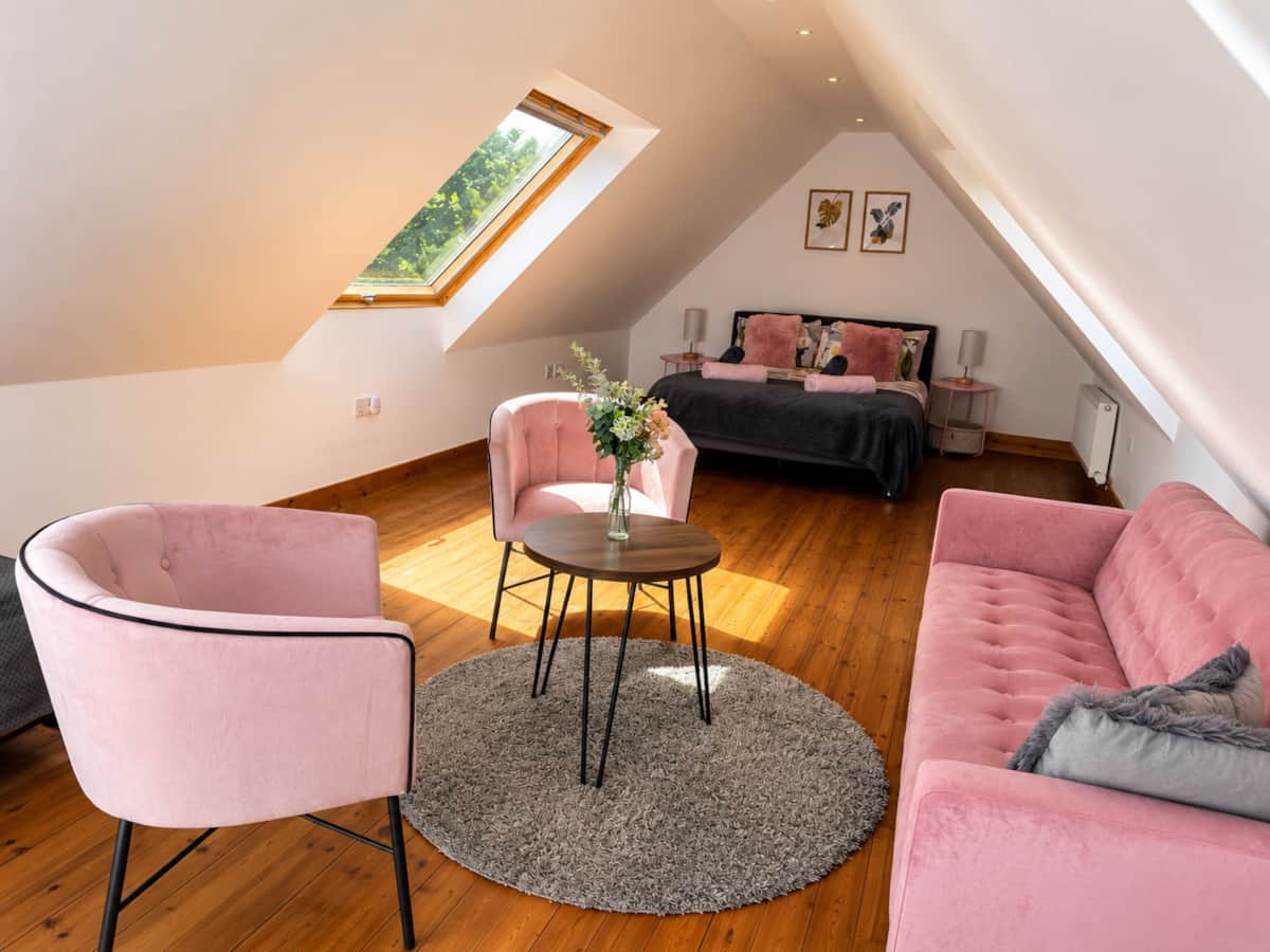 Loft bedroom under the eaves with a skylight, pink velvet chairs and sofa.