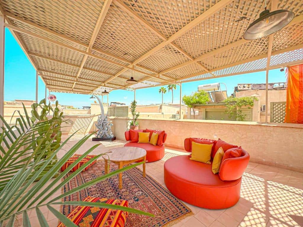 Toit-terrasse partagé avec salons colorés, pergola ombragée et ciel de Marrakech.