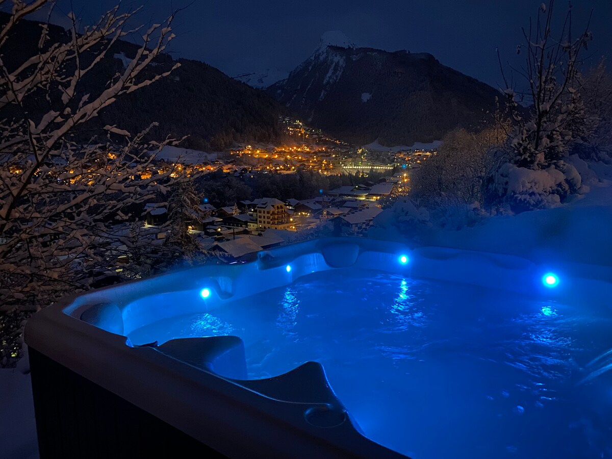 Jacuzzi illuminé la nuit, village en contrebas