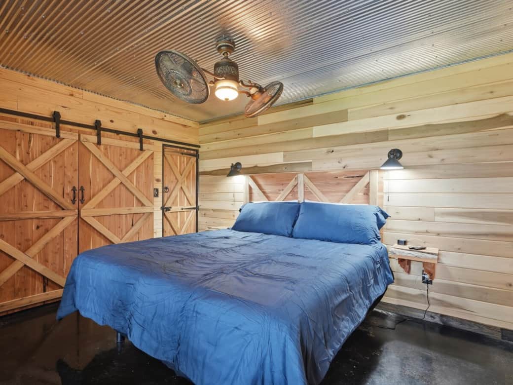 Primary bedroom features a king-size bed, double nightstands, rotating ceiling fan, sound machine, TV, spacious closet with hangers, and a sliding barn door for added privacy and a relaxing retreat.