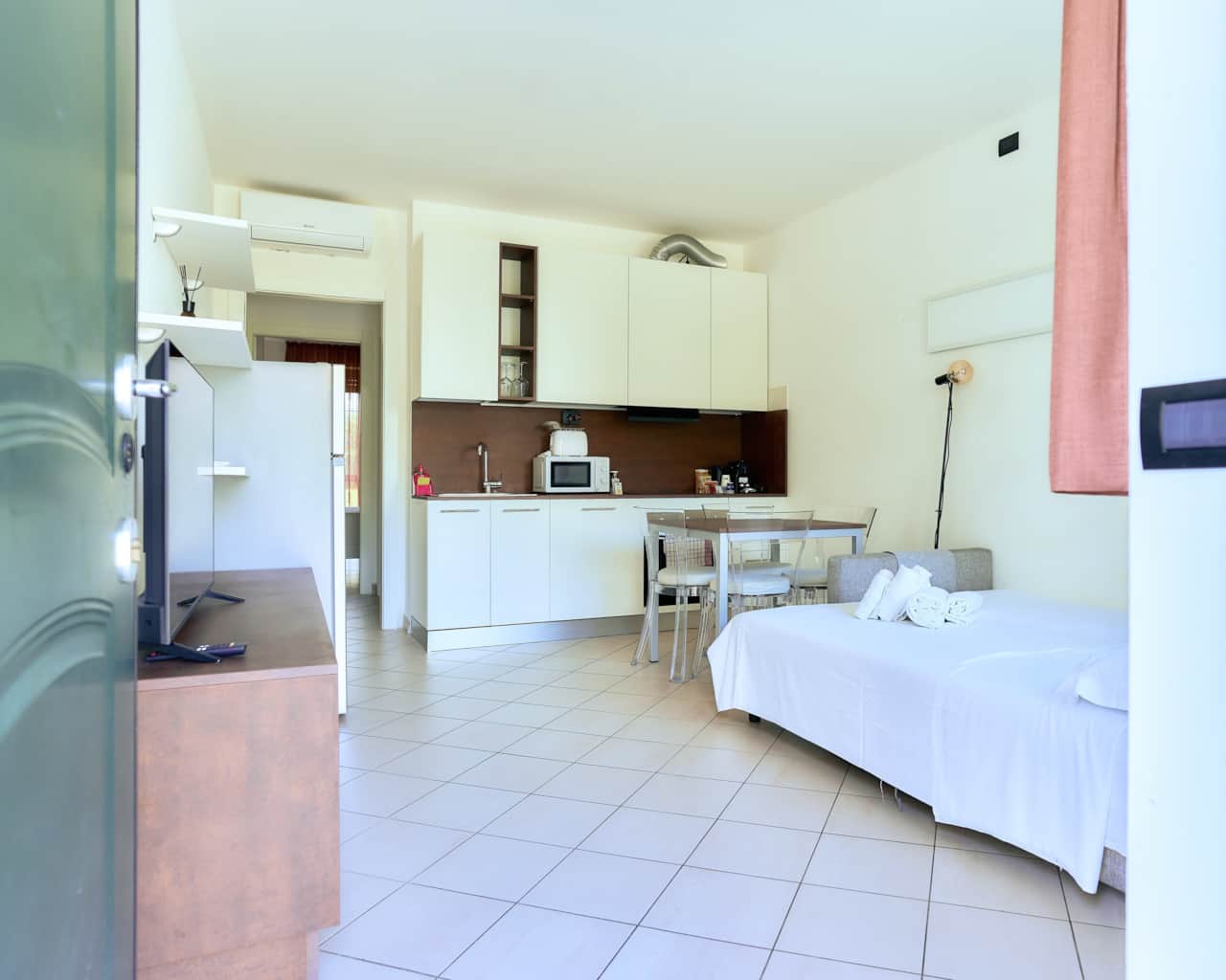 Zona de estar con cocina abierta, mesa de comedor y cama, en Monza