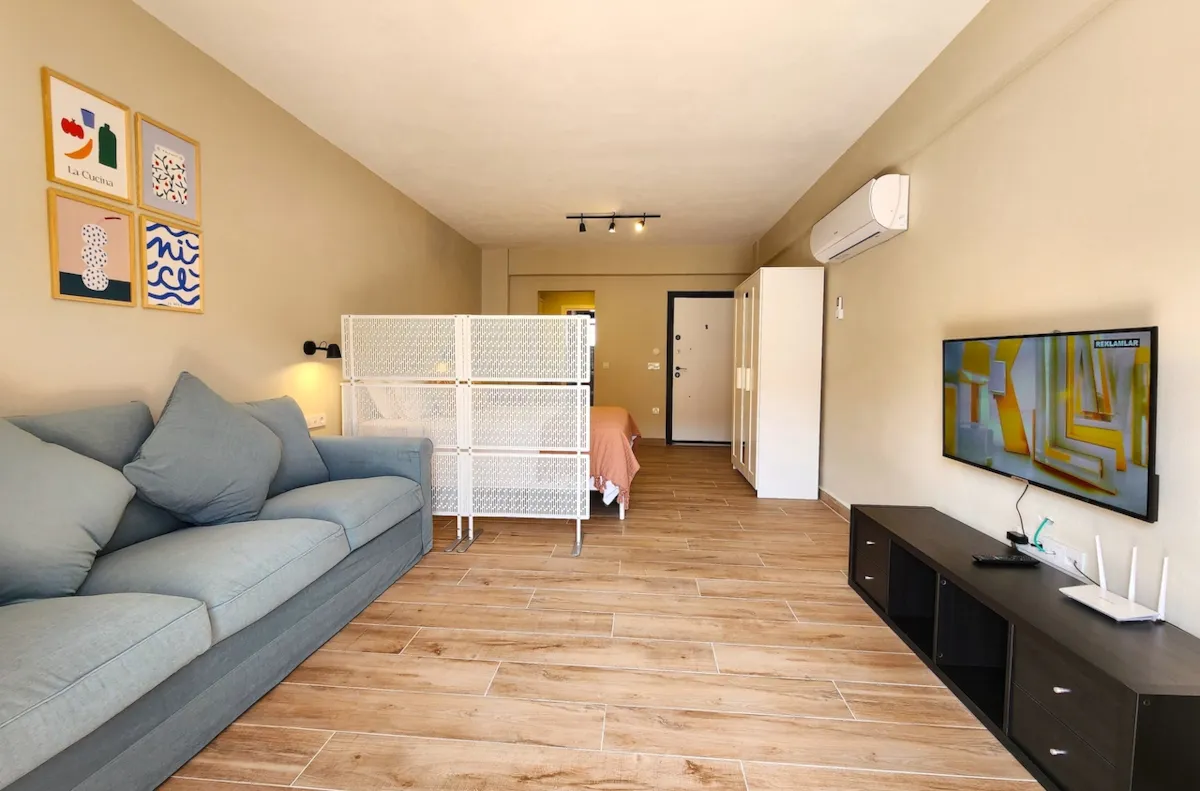 Living area with a blue sofa, a TV, and a partition separating the sleeping area in Apart Guney 8, Gocek.
