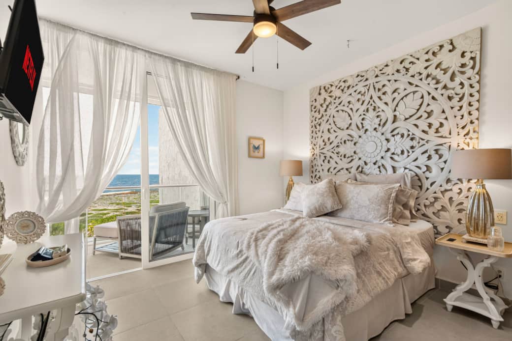 Ocean-view bedroom with a private balcony, Smart TV, AC, ceiling fan, and bedside outlets.
