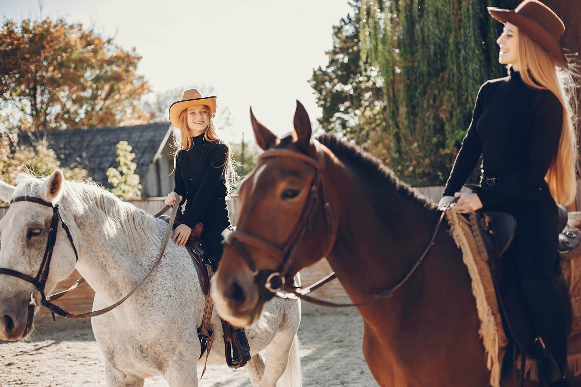 Two riders in cowboy hats on horseback at a ranch on a sunny autumn day