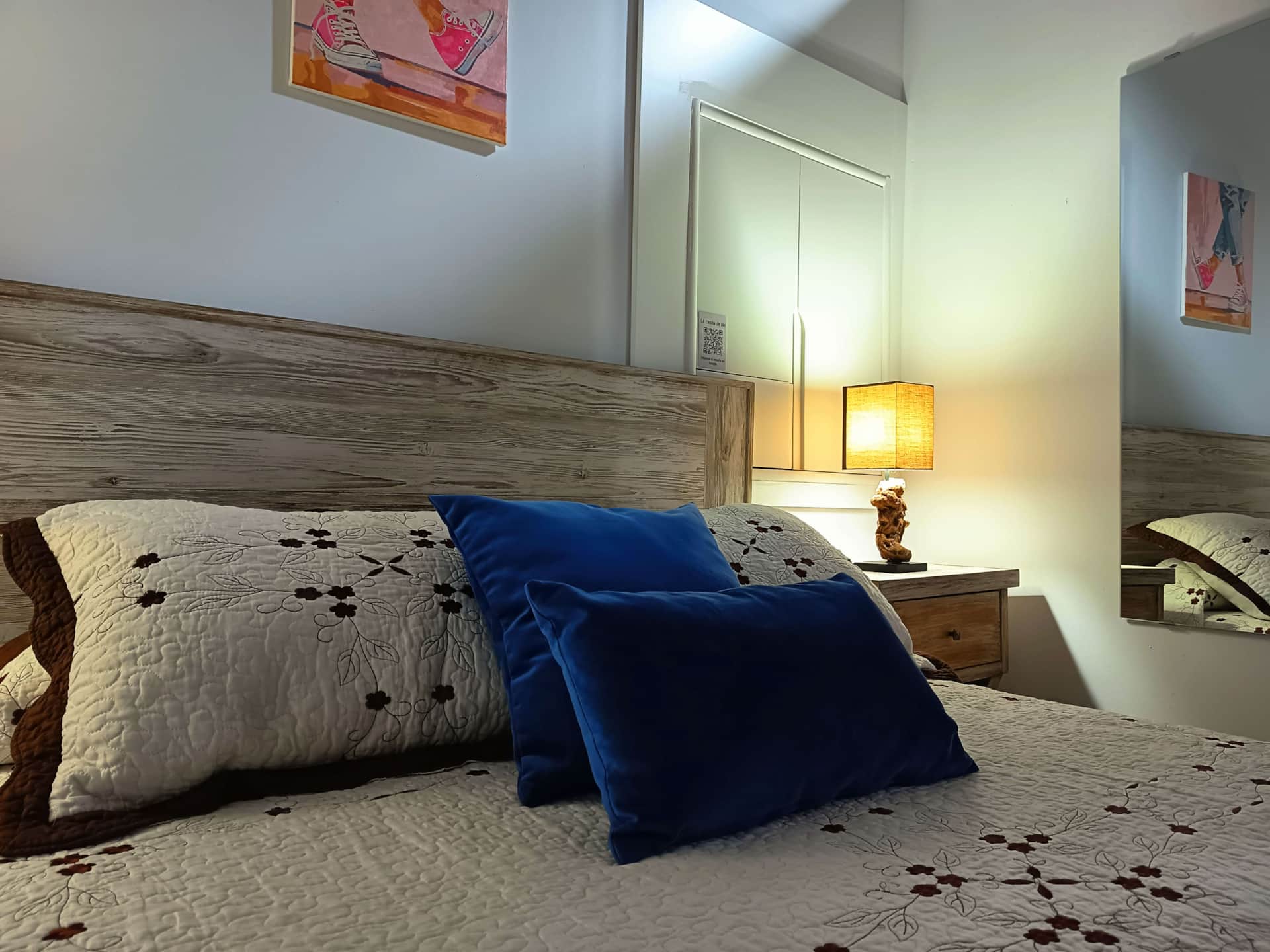 Dormitorio acogedor con cama de cabecero de madera, colcha blanca con estampado floral y cojines azules