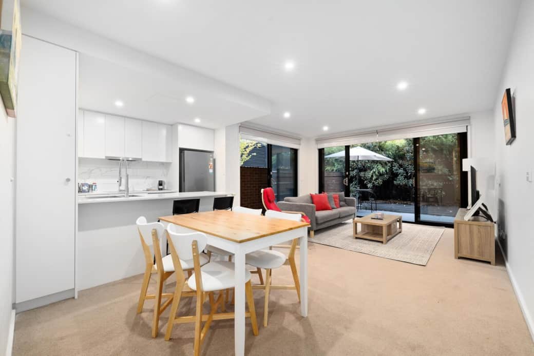  This open-plan space combines a cozy living room with a modern kitchen and dining area. The large windows flood the room with light, while the comfortable seating and stylish decor create a welcoming environment for relaxation and entertainment.