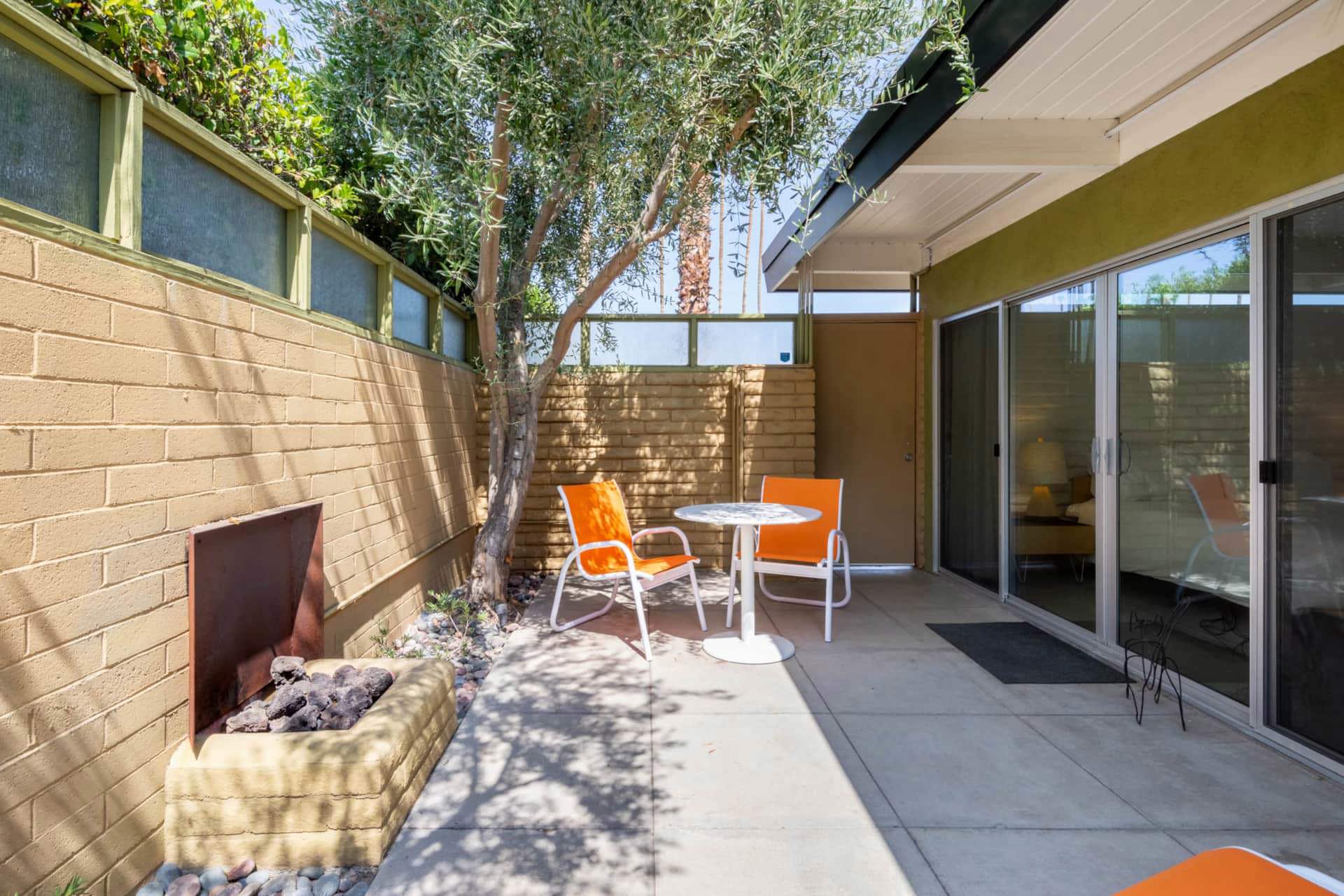 A small outdoor patio with a fireplace, two orange chairs, and a small table.