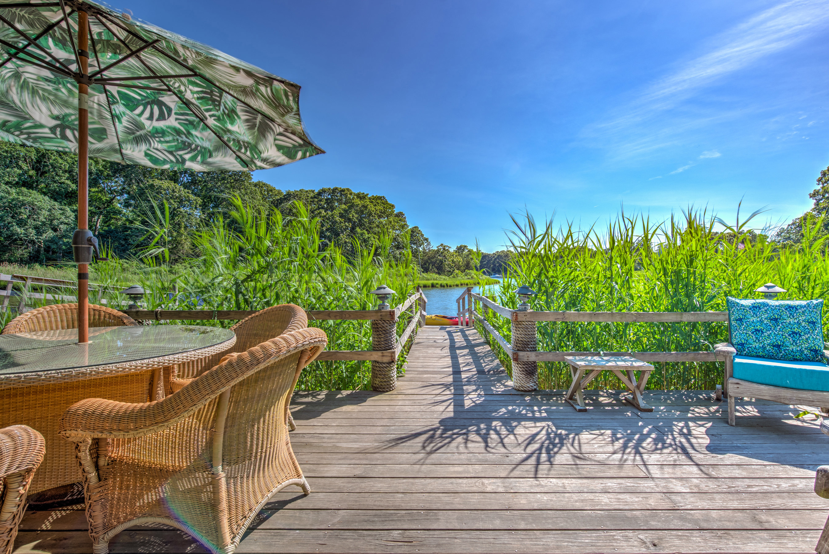 Private dock with wicker dining set, umbrella and cushioned bench among the reeds