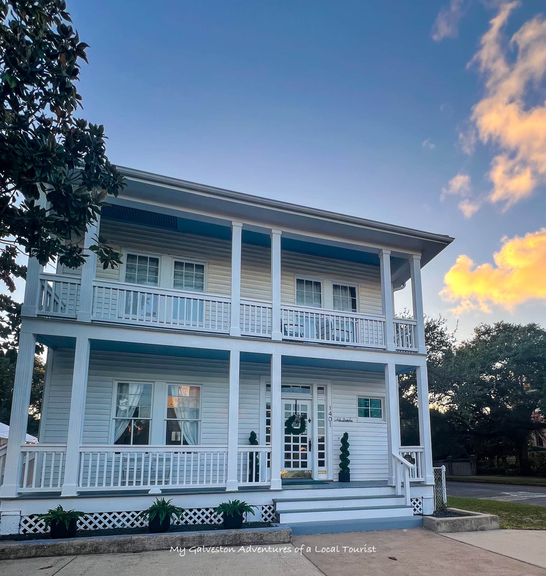 Historic 1921 exterior of White Magnolia Galveston with front porch and lush greenery
