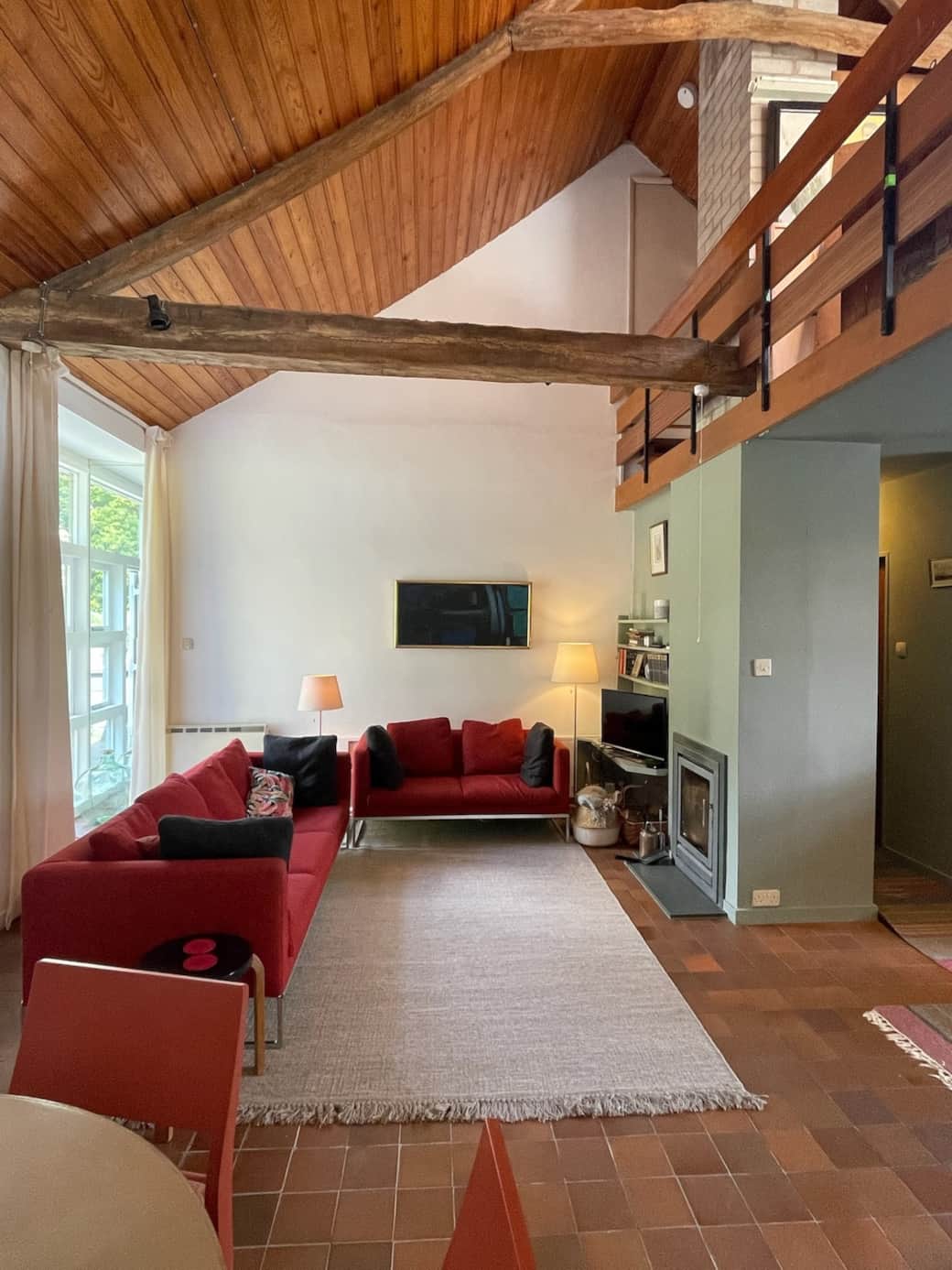 A large double height but cosy and comfortable living space with quarry floor tiles, Aalto and BBItalia furniture and stovax log burner with original artwork. A spiral  stair leads to the mezzanine with views east across the valley