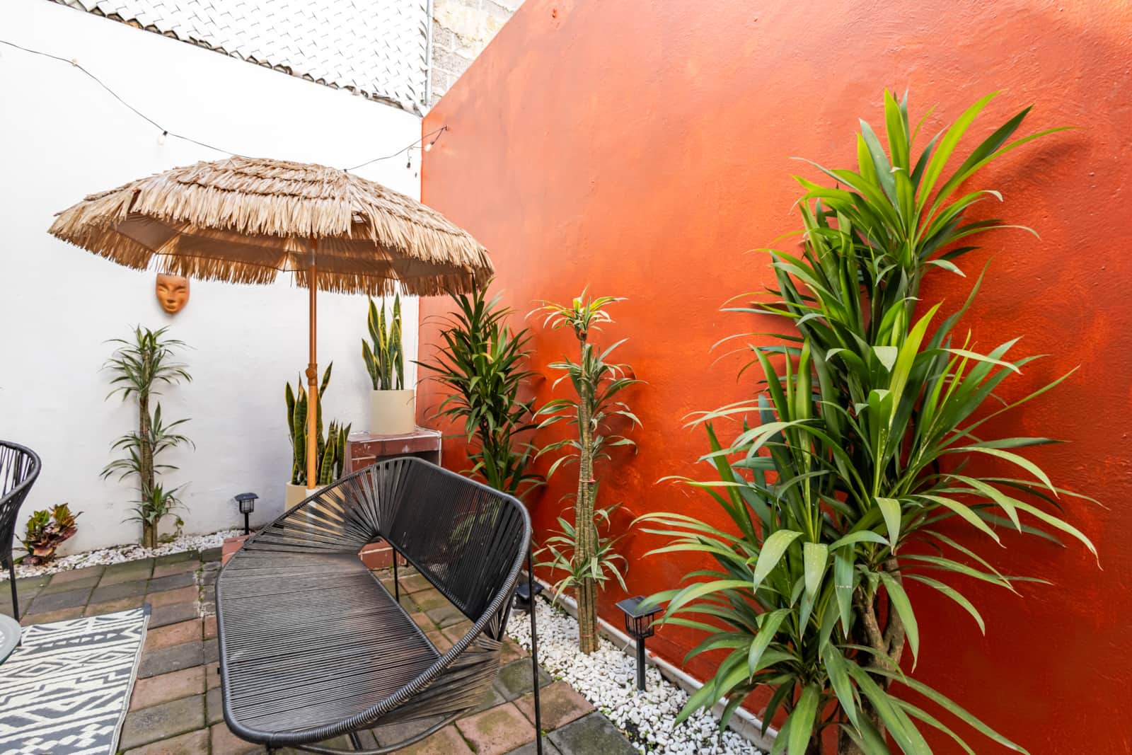 Jard&iacute;n interior con sombrilla de palapa y muro de terracota en Casa Atlixco