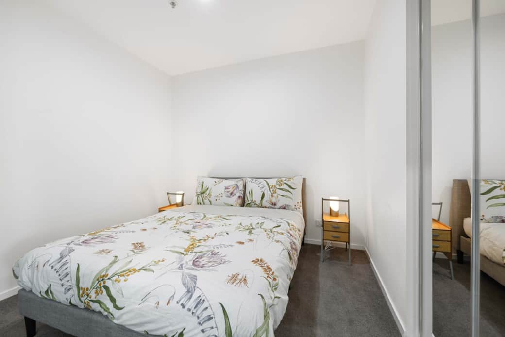 The bedroom is simply designed, with a large bed dressed in a floral duvet that adds a touch of nature to the room. The soft lighting and minimalist decor create a tranquil space, ensuring a comfortable stay. A perfect sanctuary for relaxation.