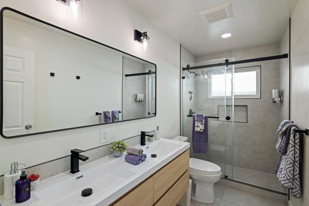Bright bathroom with double sinks, large mirror, and glass shower.