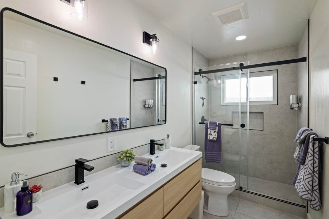 Bright bathroom with double sinks, large mirror, and glass shower.