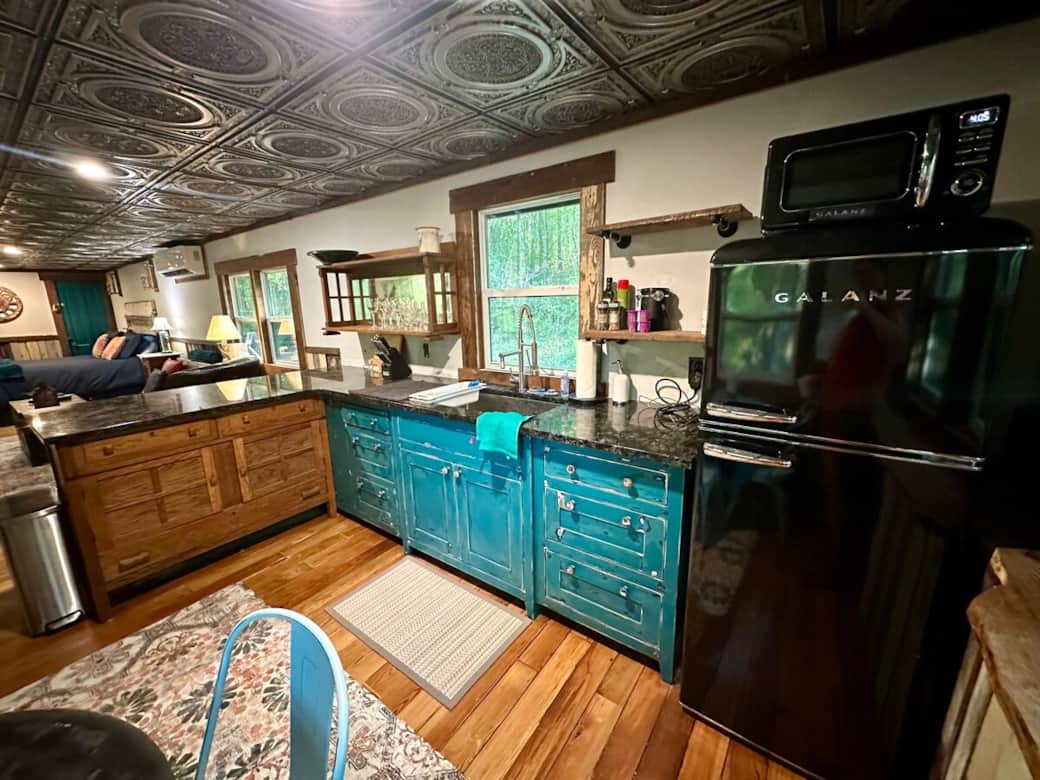 Our custom teal kitchen features flush inset cabinets with funky steampunk themed knobs, a retro black fridge and microwave, and a 1920 white oak server, all topped with flashy granite winking blue opals.  We have pots and pans, and all the dishes. 