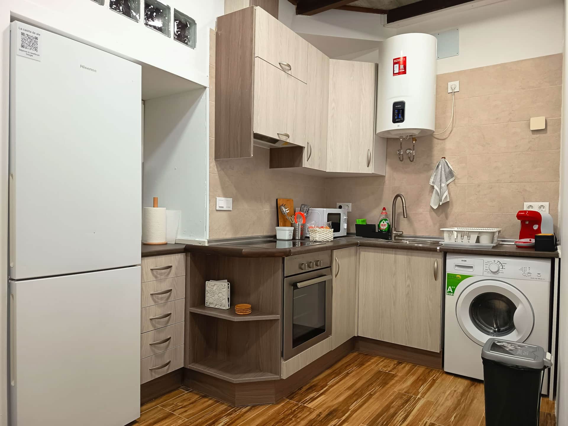 Cocina equipada con nevera, horno, vitrocerámica, fregadero, lavadora y cafetera en un espacio moderno y funcional