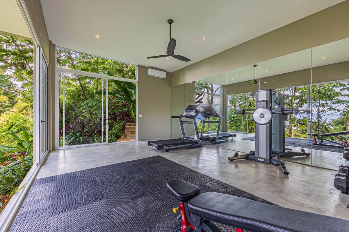 Private gym at Villa Sueño with panoramic jungle views through floor-to-ceiling glass walls.