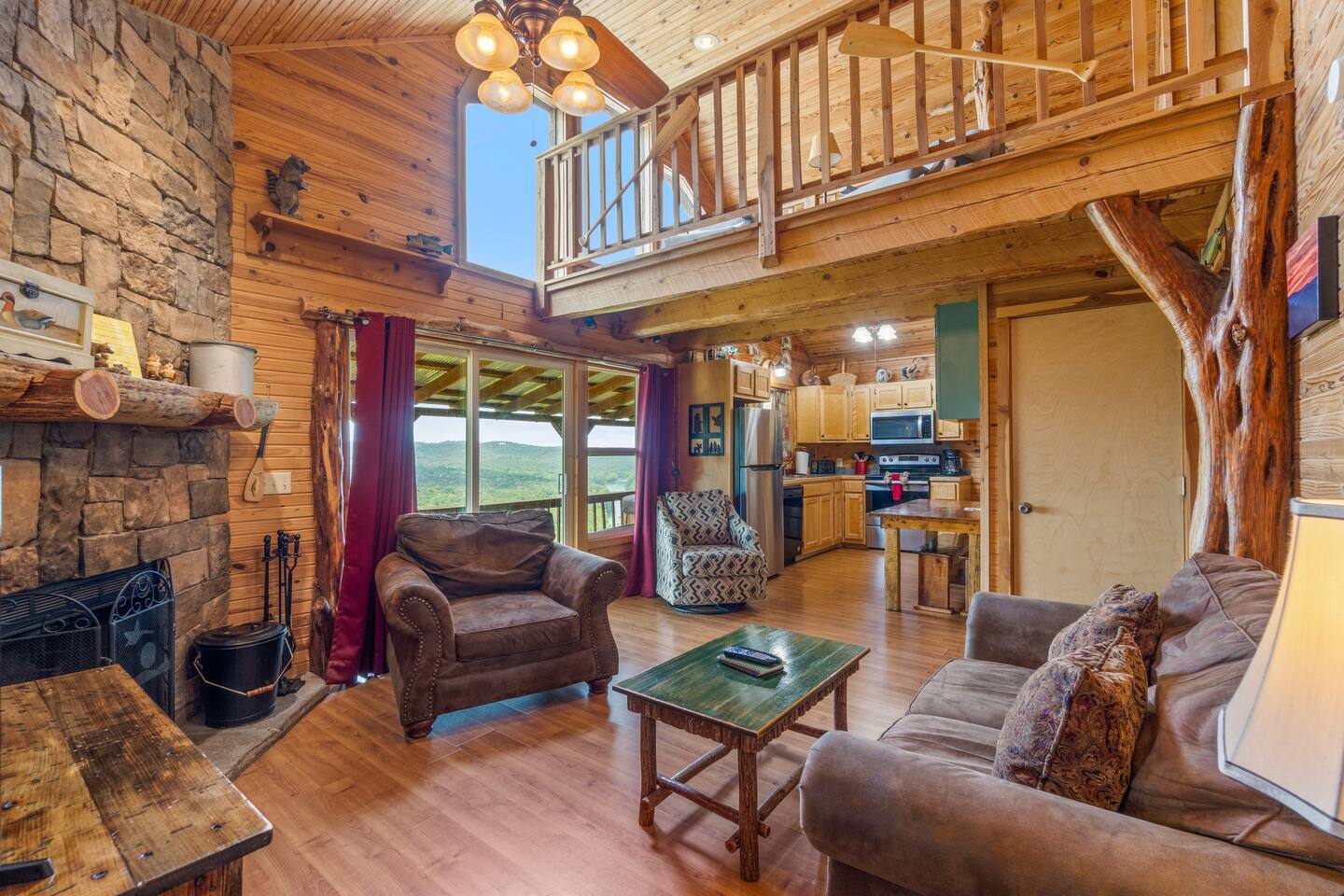 A wide view of a cozy living room with a stone fireplace, wooden beams, and a loft area.