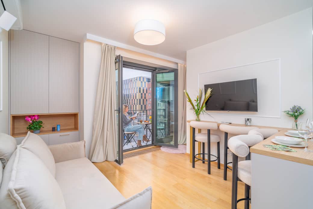 Nowoczesny salon z aneksem i balkonem, jasny, przytulny, urządzony w neutralnych barwach.