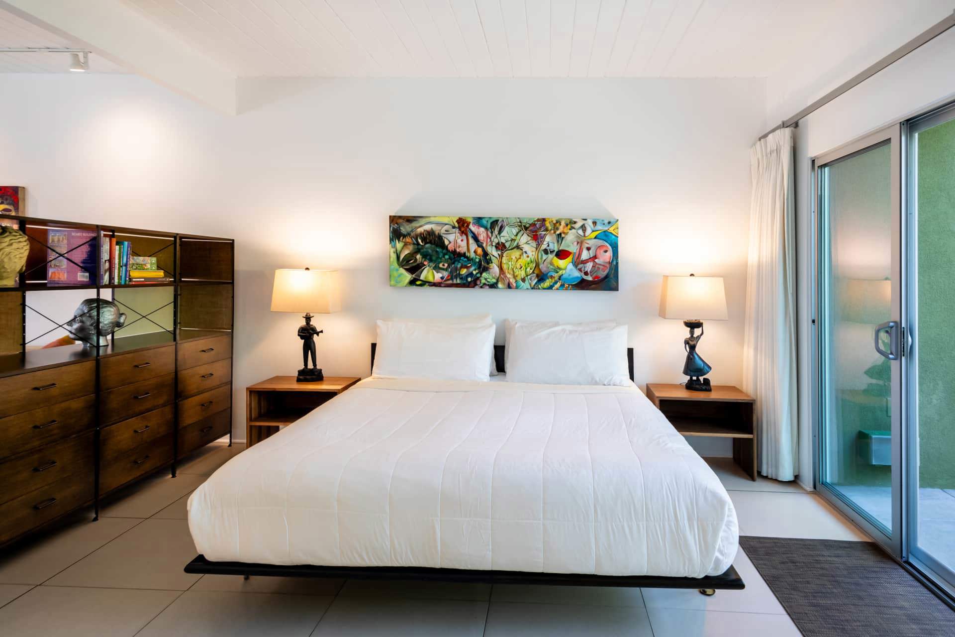 A hotel room with a large bed, two nightstands, and a colorful piece of artwork above the bed.