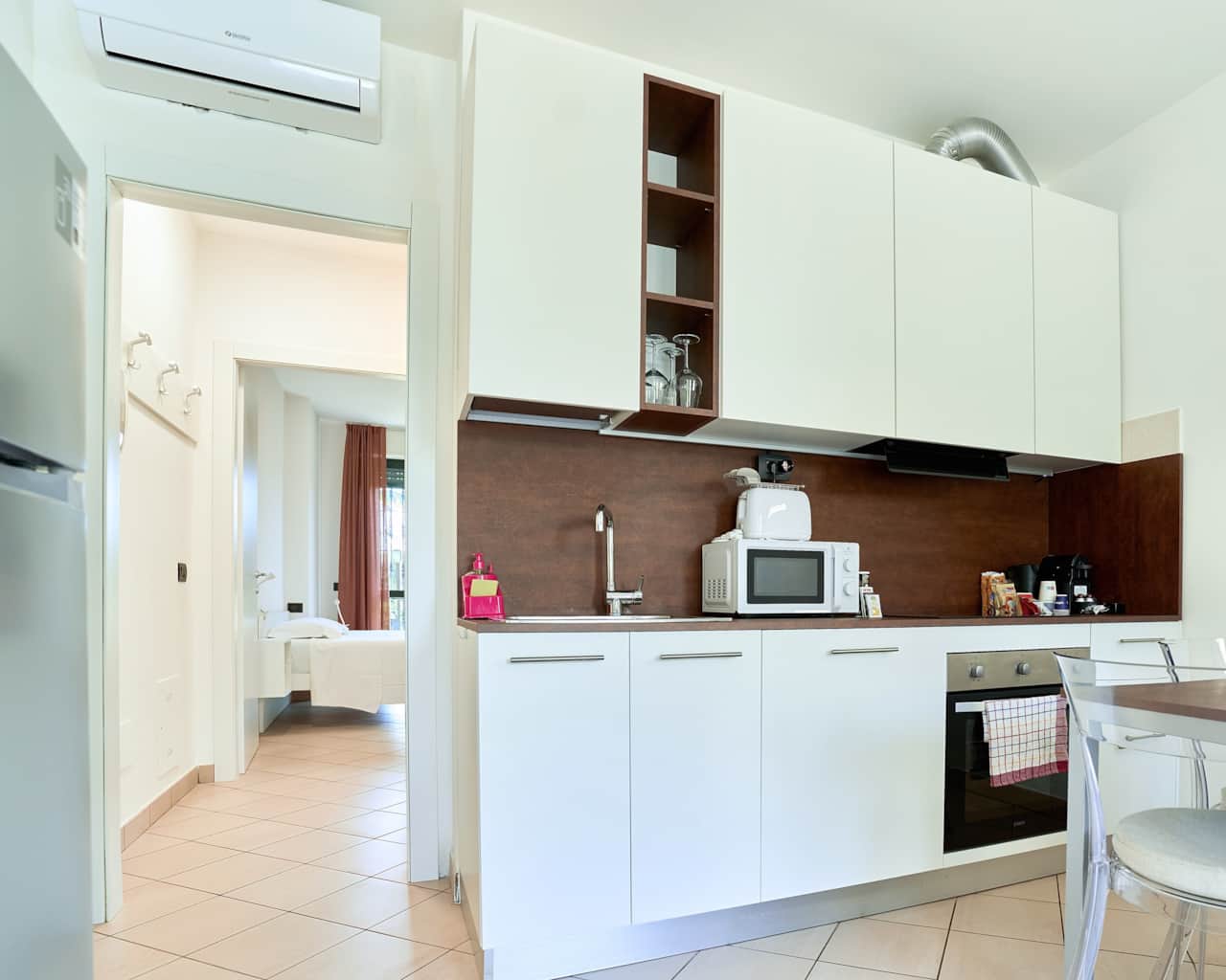 Cocina con placa, horno, microondas y armarios altos blancos