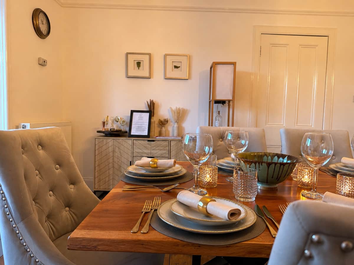 Dining table laid for dinner with candles, glassware and gold napkin rings.