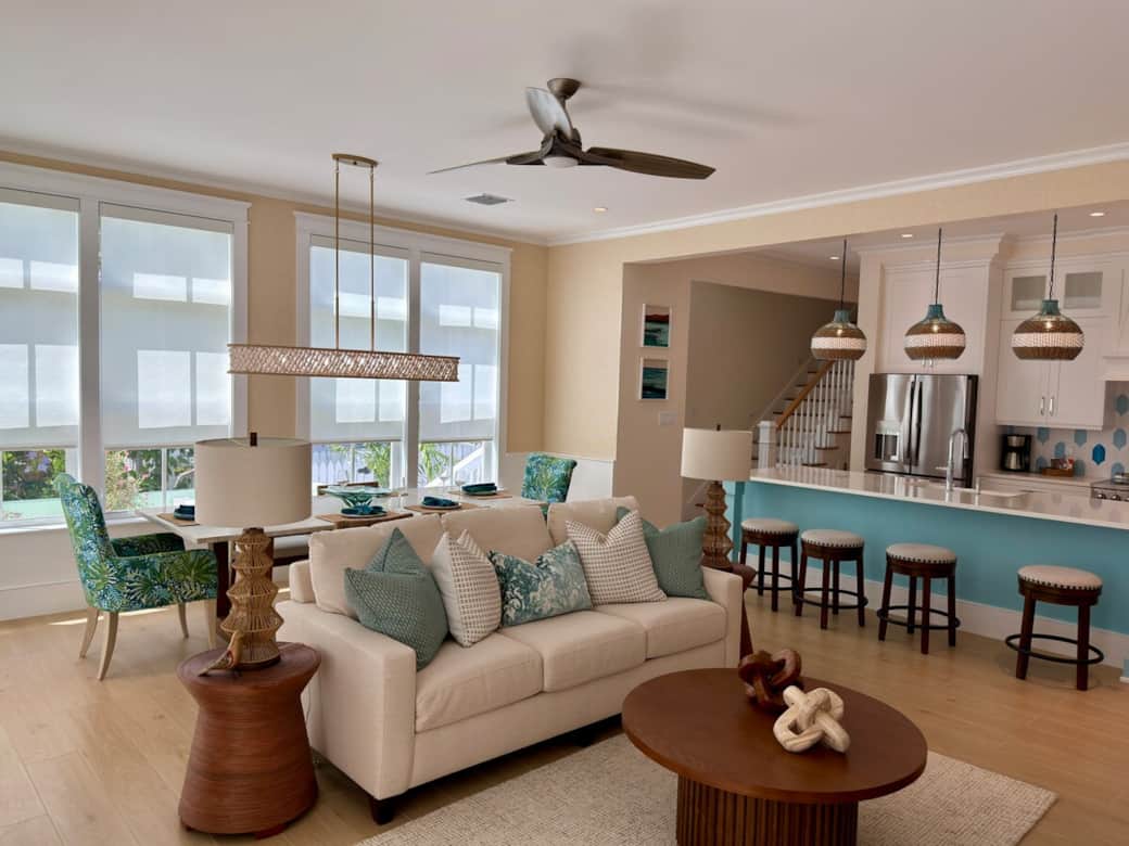 A bright, coastal-modern gathering space with an open layout that flows into the kitchen and dining area. Comfortable seating, natural light, and two double doors open directly to the pool for easy indoor-outdoor living.