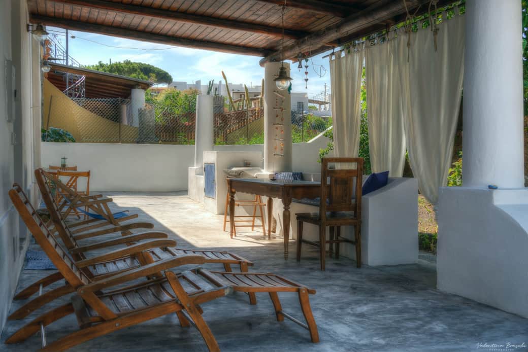 Veranda eoliana con lettini prendisole, tavolo in legno e zona relax immersa nel verde