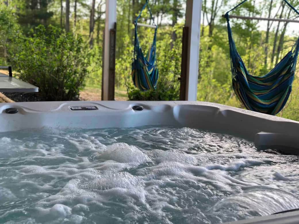 6-person year-round hot tub bubbling under the covered porch — hammock chairs behind. Other seating on both sides.

hot tub, jacuzzi, six-person hot tub, hammock chairs, covered hot tub, year-round soaking, relaxation amenity, Smith Mountain Lake.
