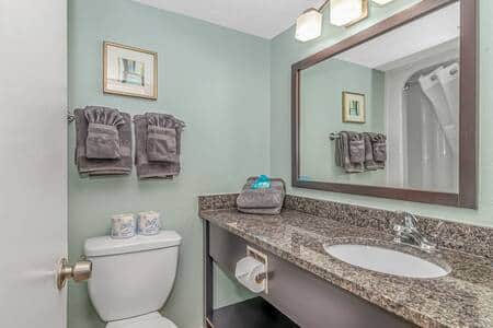 Updated bathroom with granite countertop, large mirror, and fresh guest amenities.