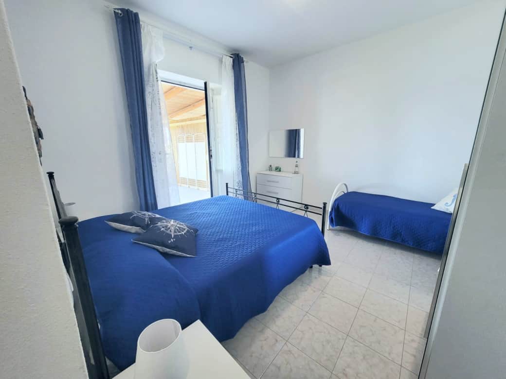 Camera luminosa con letti blu e accesso al patio a Casetta Faraglione