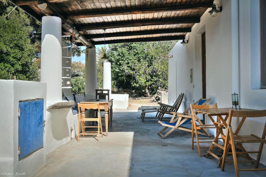 Veranda coperta in stile eoliano con tavoli in legno e area relax immersa nel verde