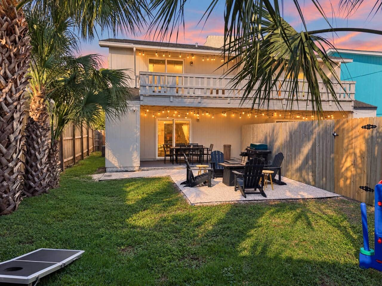 Enjoy a fenced backyard with a fire pit, BBQ grills, and covered outdoor dining beneath string lights. Upstairs, the king suite opens onto its own covered balcony with cushioned seating, giving you another spot for coffee or a quiet evening