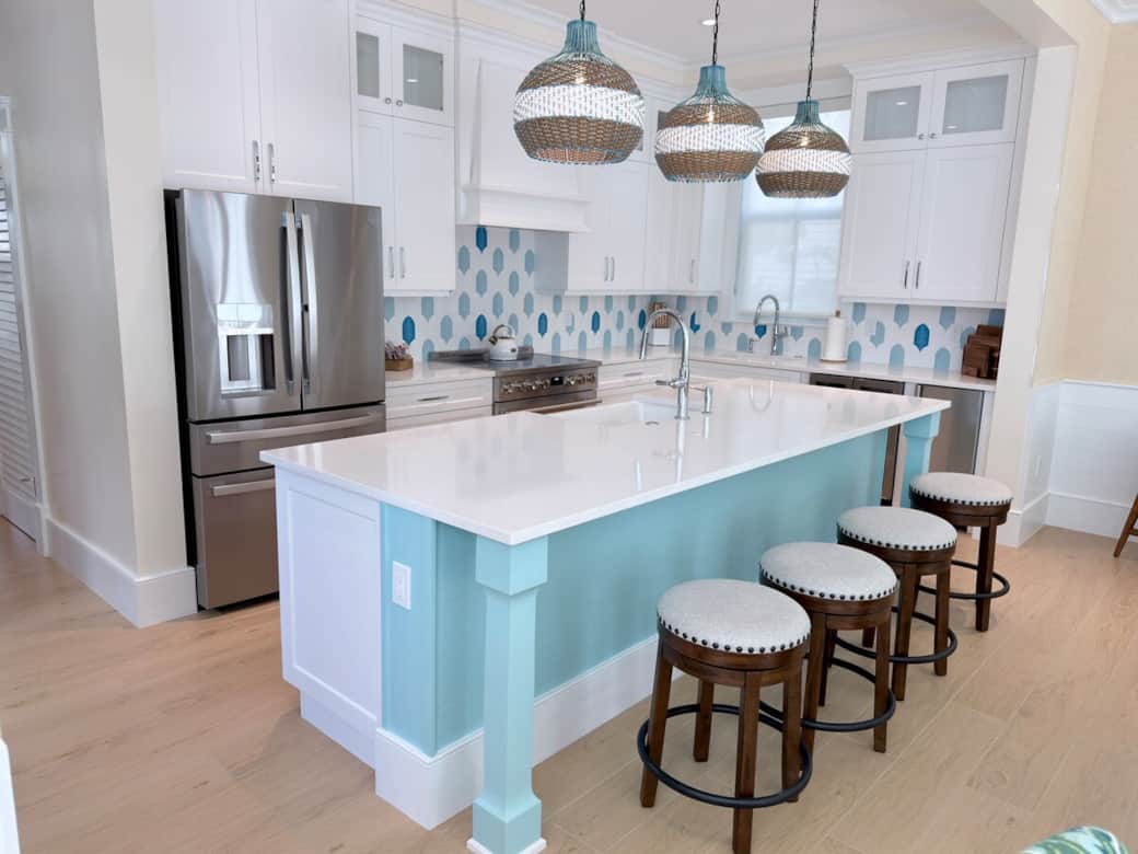 A bright coastal-modern kitchen with a large island, seating for 4, and a double farmhouse sink. Its open-concept layout flows into the dining and family room, creating an airy and inviting main gathering space.