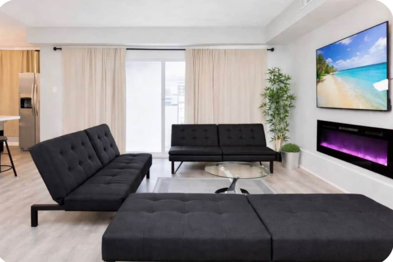 Bright, modern living room with three futon sofa beds, an electric fireplace, and a wall-mounted flat-screen TV.
walk out balcony behind the sofa.